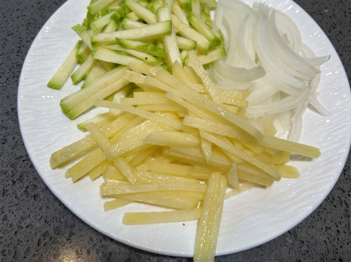 Fines lamelles de courgette, doignon et de pomme de terre sur une assiette blanche.
