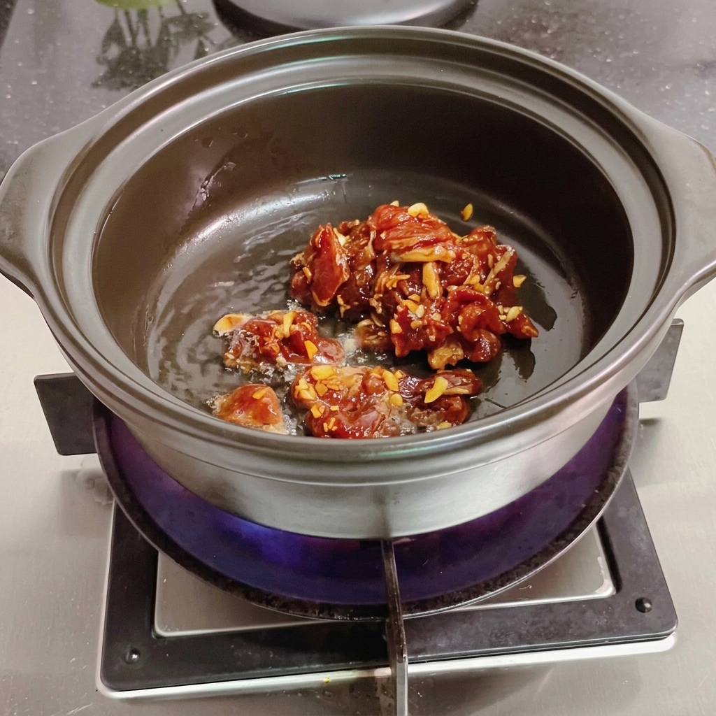 Tranches de viande remuées dans un pot en terre cuite avec une spatule en bois.