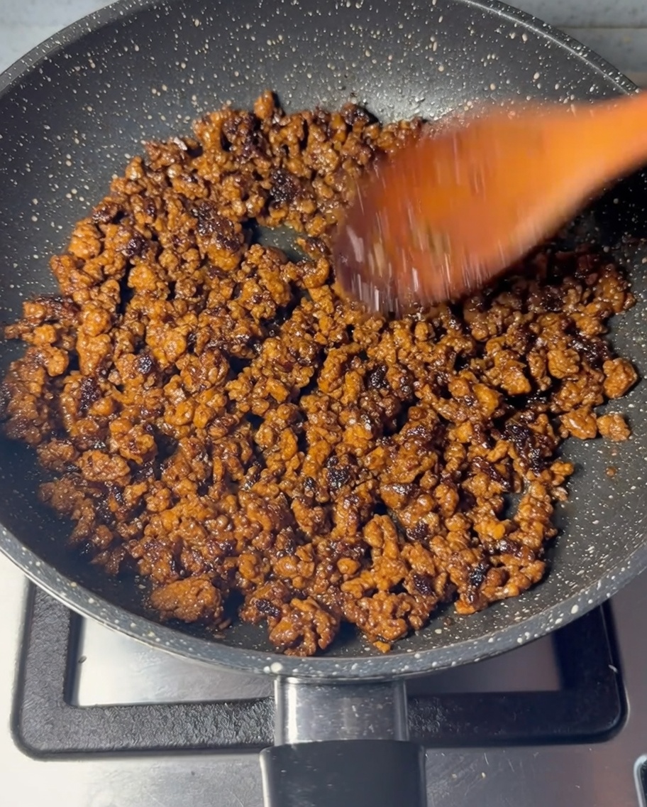 Bœuf haché en train de revenir dans une poêle avec une spatule en bois.