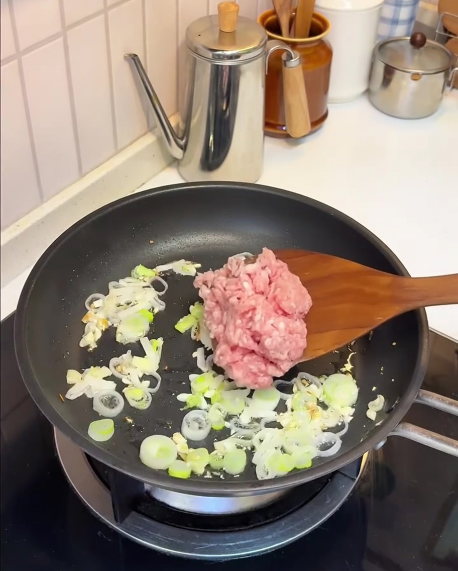 Porc haché en train de sauter dans une poêle avec de lail et des oignons verts.