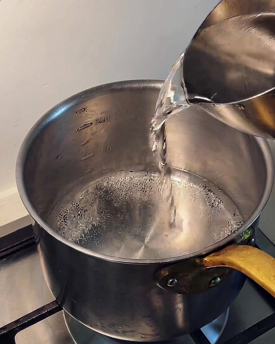 Verser de leau claire et froide dune carafe en métal dans une casserole en inox sur une plaque de cuisson.