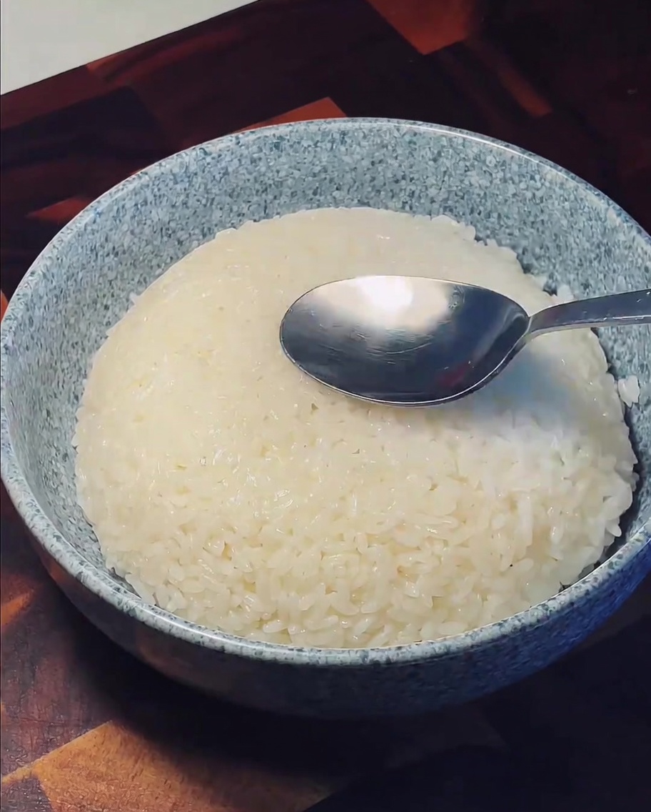 Une cuillère en métal pressant le centre dun tas de riz blanc moelleux dans un bol en céramique.