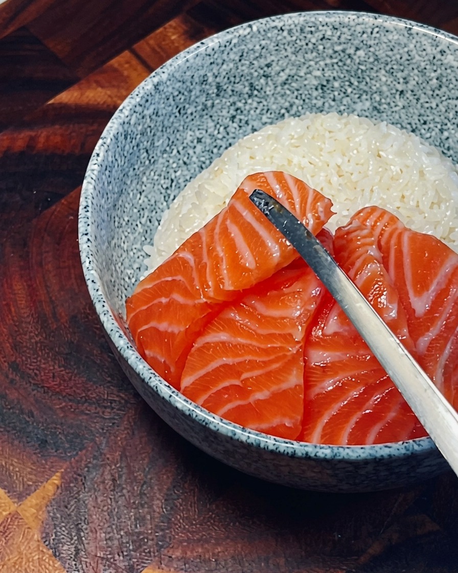 Des tranches de saumon frais, orange vif, disposées en cercle chevauchant sur le riz blanc.