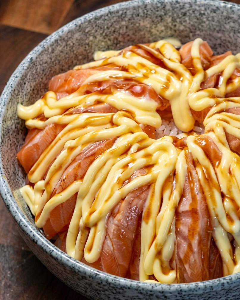 Un bol de riz au saumon nappé de sauce teriyaki sombre sur la couche de mayonnaise.