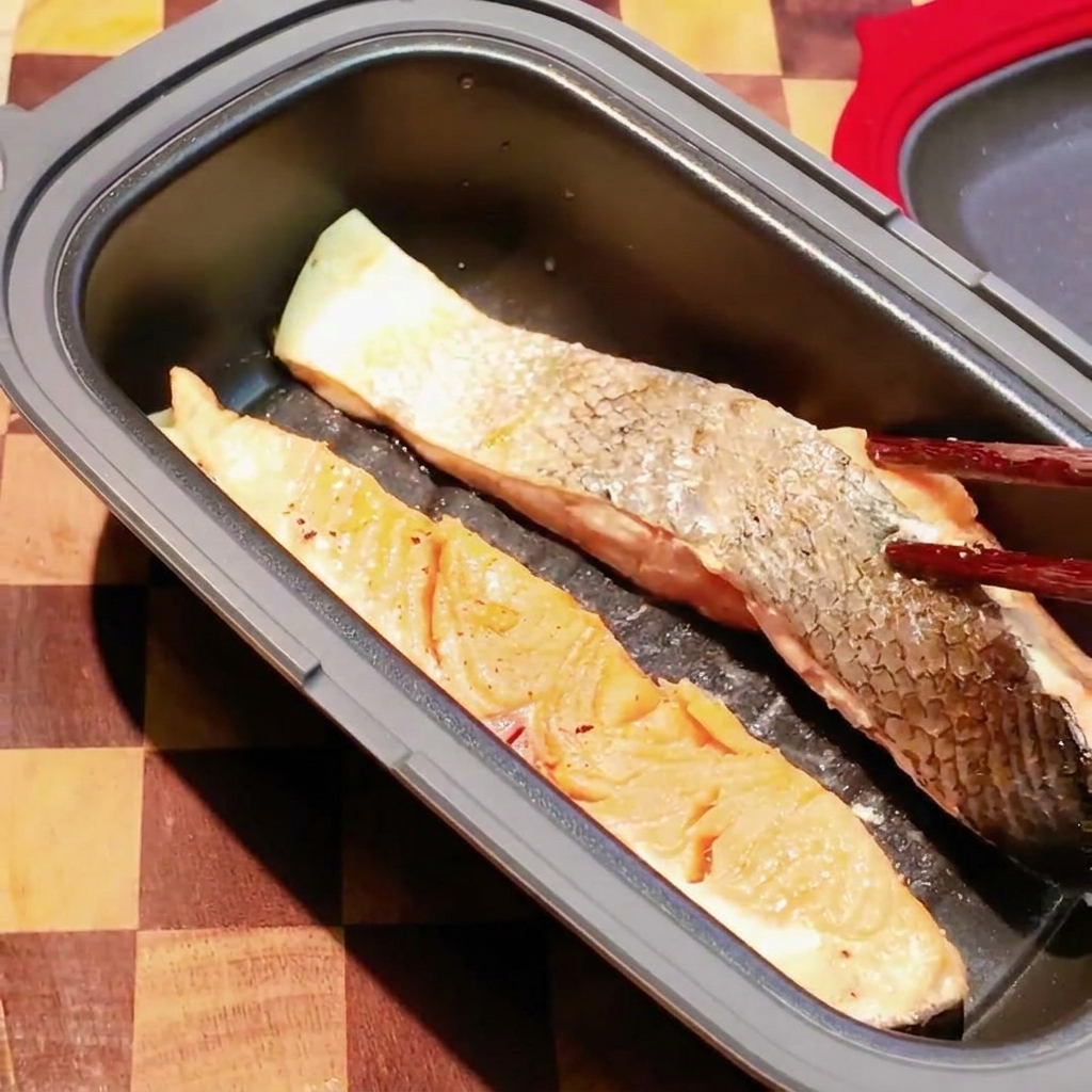 Des baguettes retournant un filet de saumon partiellement cuit dans une poêle sombre pour micro-ondes.