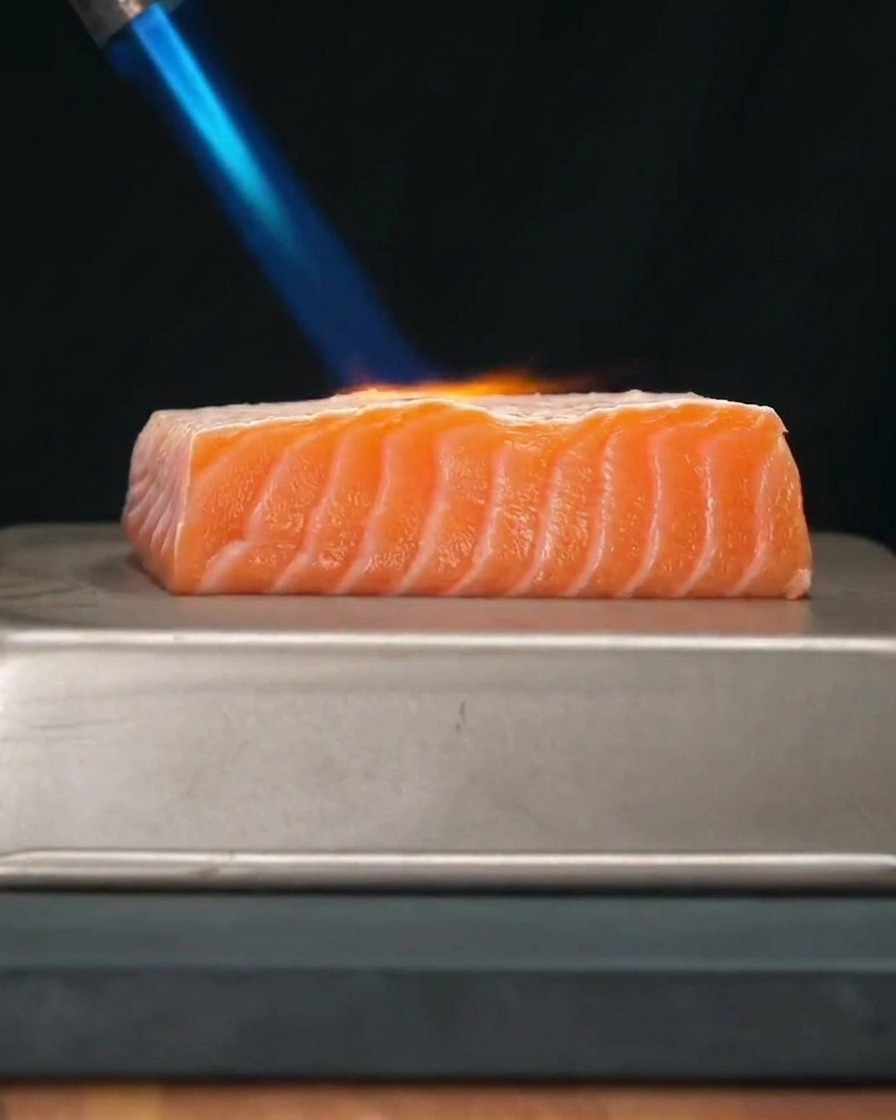 Un filet de saumon frais et épais en cours de saisie avec la flamme bleue vive dun chalumeau de cuisine.