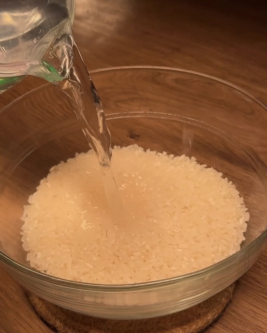De leau est versée dun verre doseur dans un bol en verre rempli de riz blanc.
