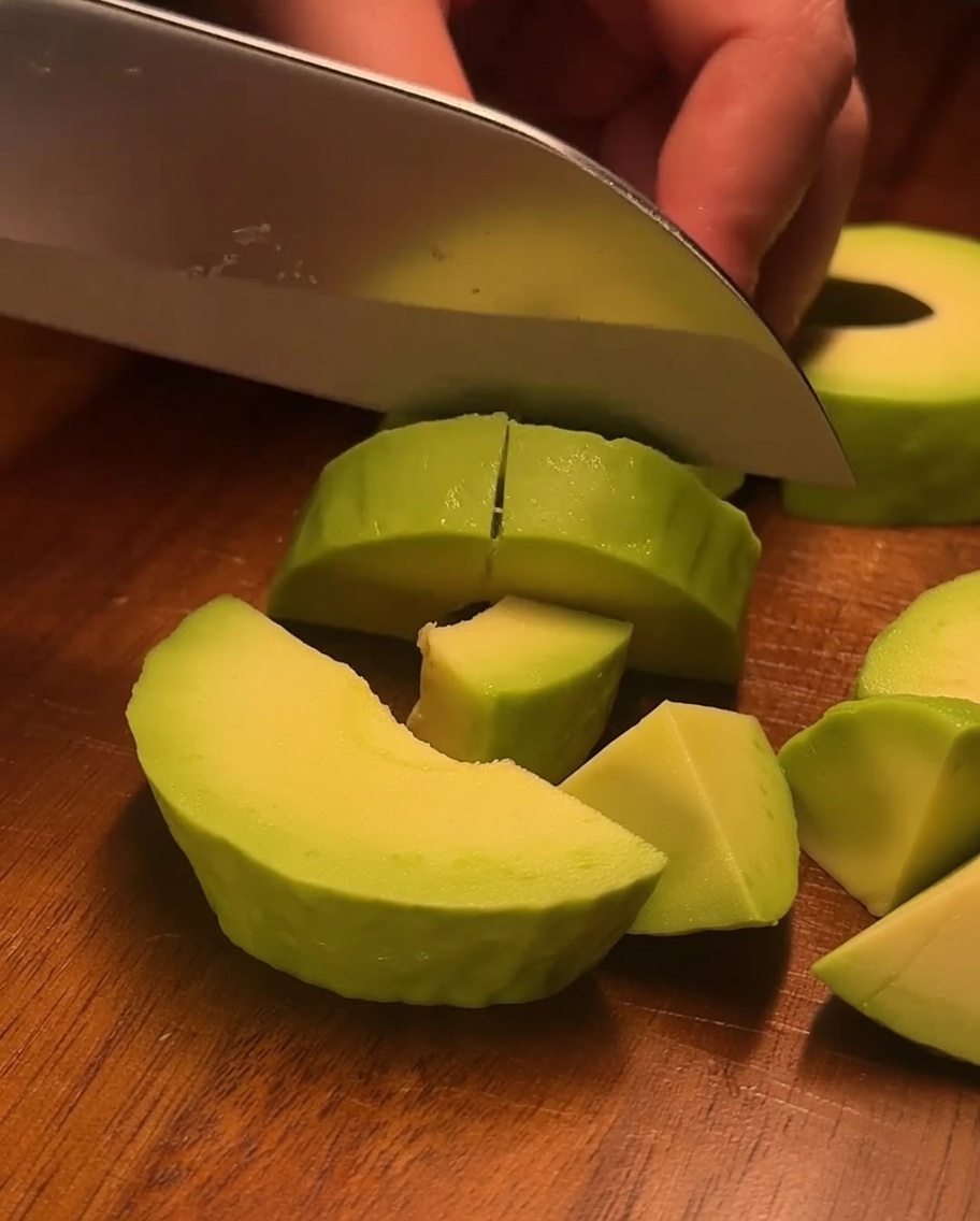 Des crevettes cuites sont coupées en petites bouchées sur une planche en bois.