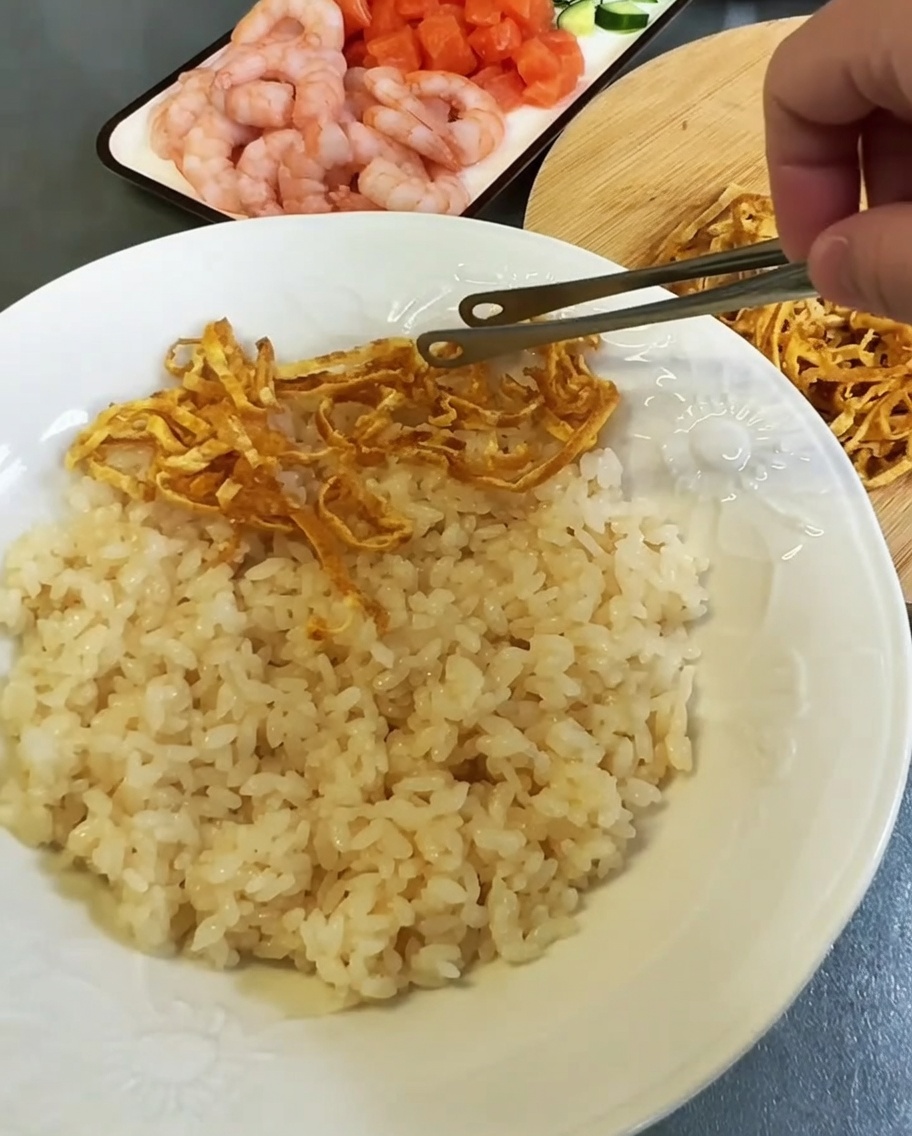 Disposition de lanières dœuf colorées et de garnitures de fruits de mer sur un lit de riz dans une assiette blanche.