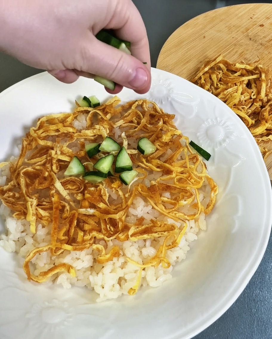 Dés de concombre vert saupoudrés sur la couche de riz vinaigré et de lanières dœuf.