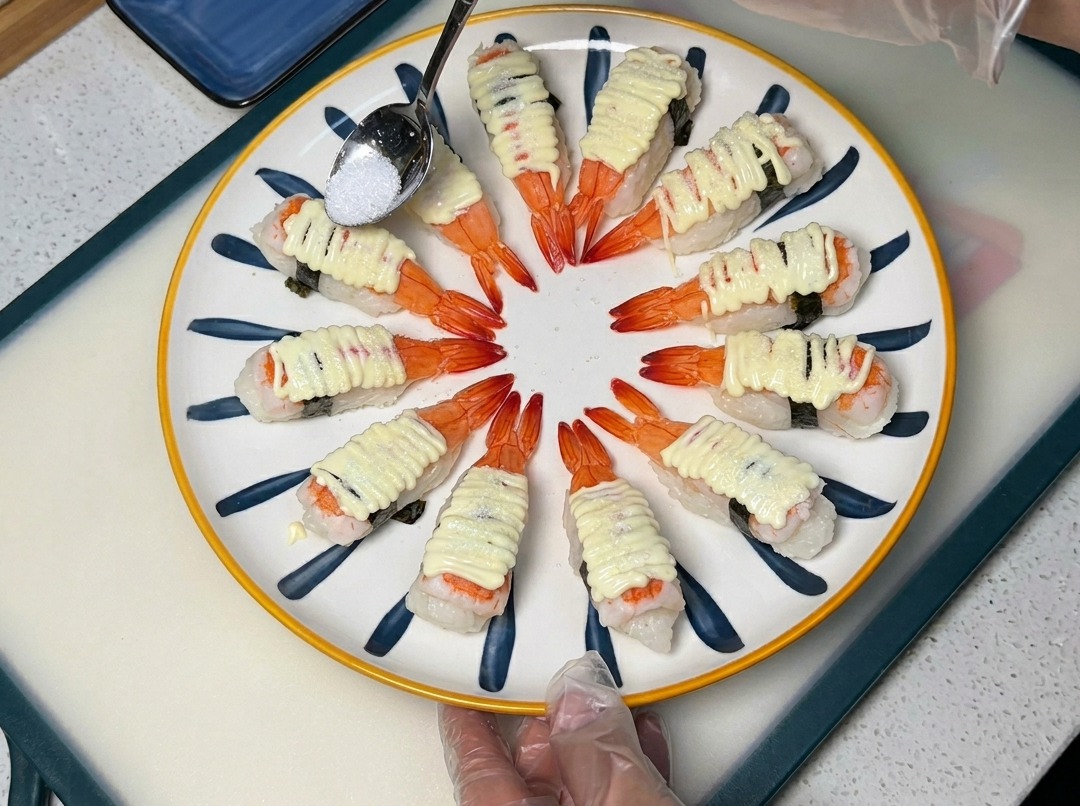 Une cuillère saupoudrant du sucre sur les sushis à la mayonnaise dans une assiette décorative.