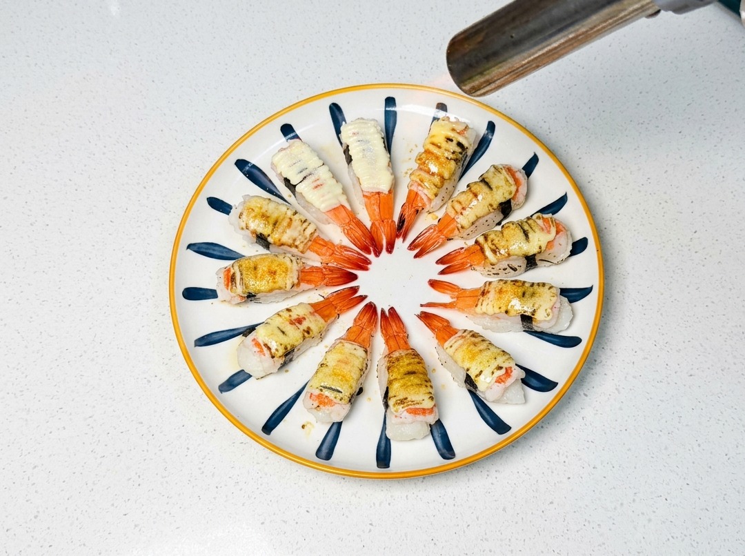 Un chalumeau de cuisine brunissant le sucre et la mayonnaise sur des sushis aux crevettes.