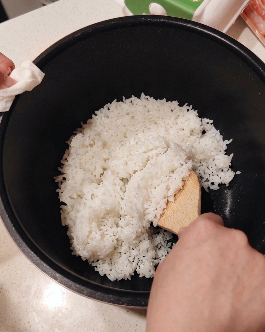 Incorporation du vinaigre à sushi dans le riz blanc fraîchement cuit à laide dune spatule en bois.