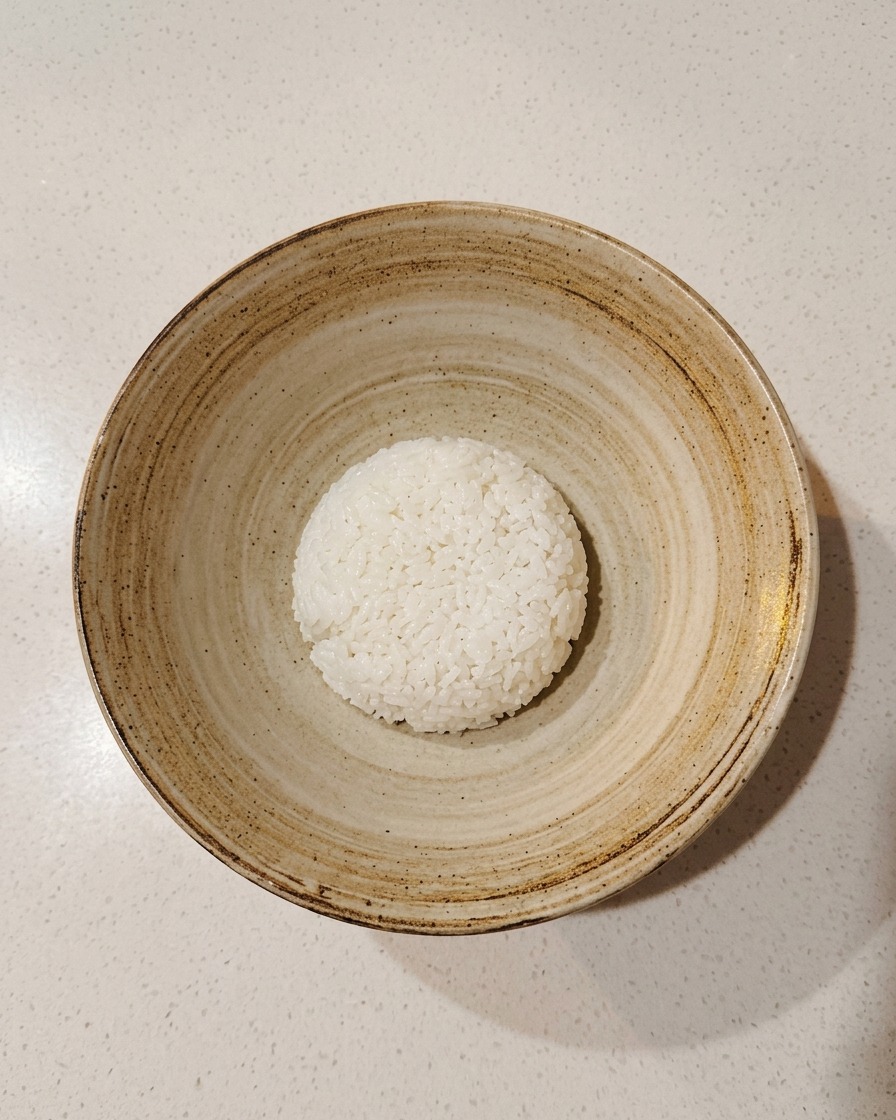 Une portion de riz à sushi assaisonné placée au centre dun bol en céramique rustique.