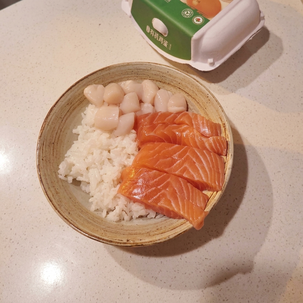Bol rempli dune base de riz à sushi, garni dune disposition soignée de tranches de saumon, de Saint-Jacques et de crevettes sucrées.