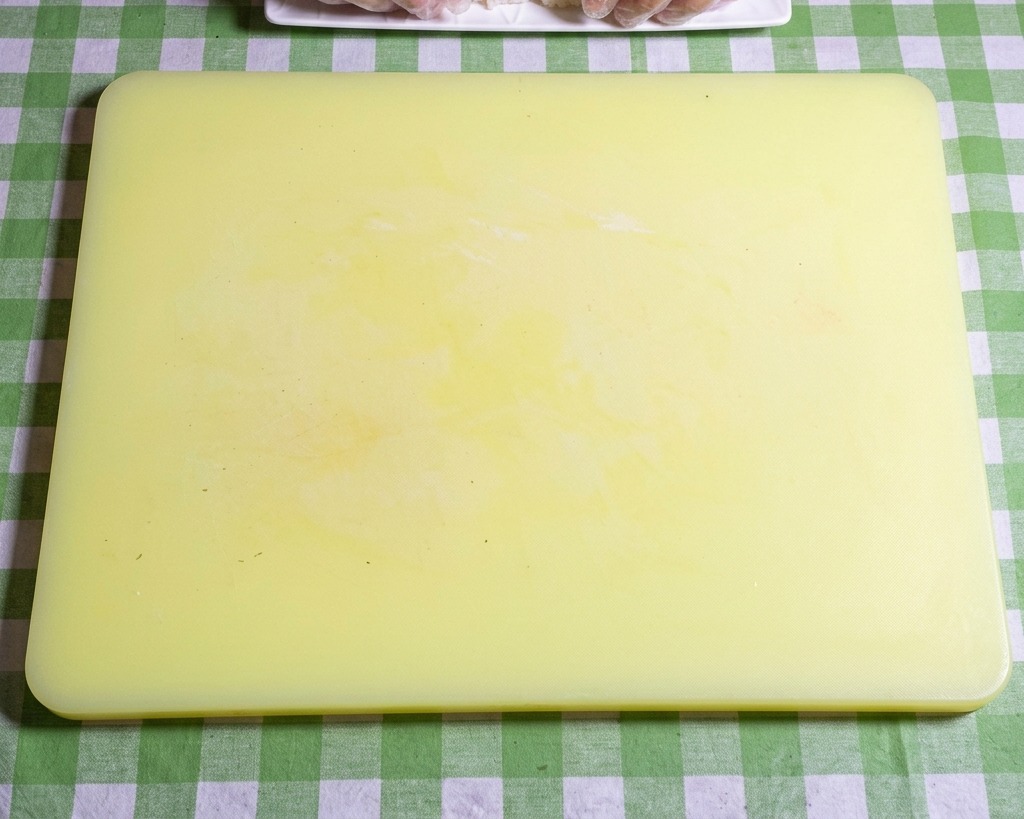 Gros plan sur des mains gantées façonnant du riz à sushi gluant en boules ovales uniformes sur une planche à découper jaune.
