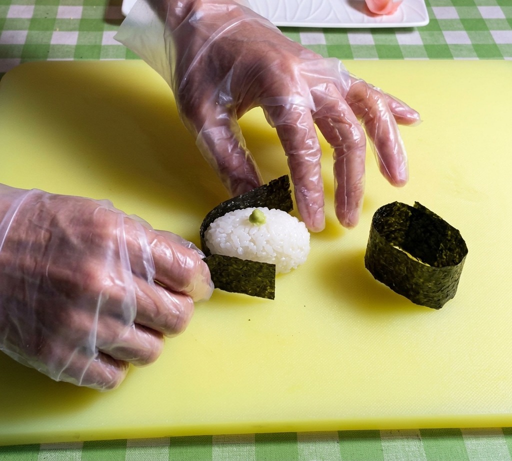 Mains plaçant une bande de nori sombre autour du bord dune base de riz à sushi ovale.