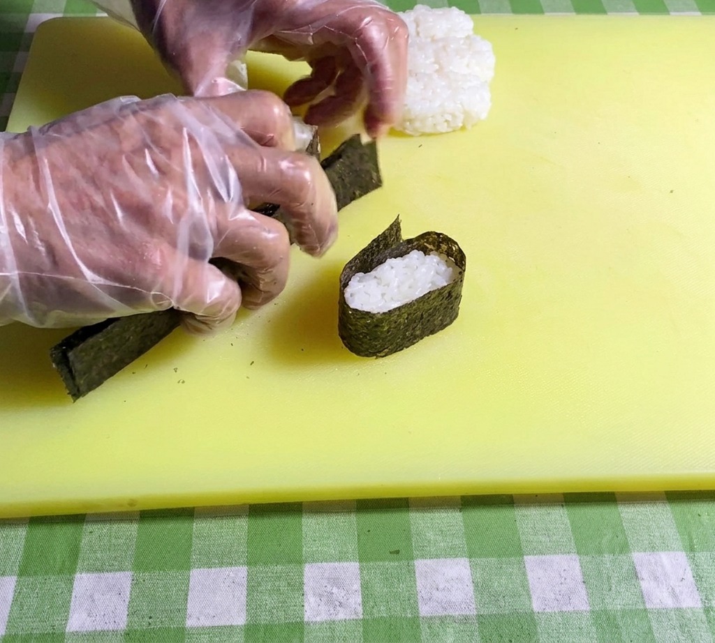 Gros plan sur des mains pressant les extrémités dune bande de nori pour la fixer autour dune base de riz.
