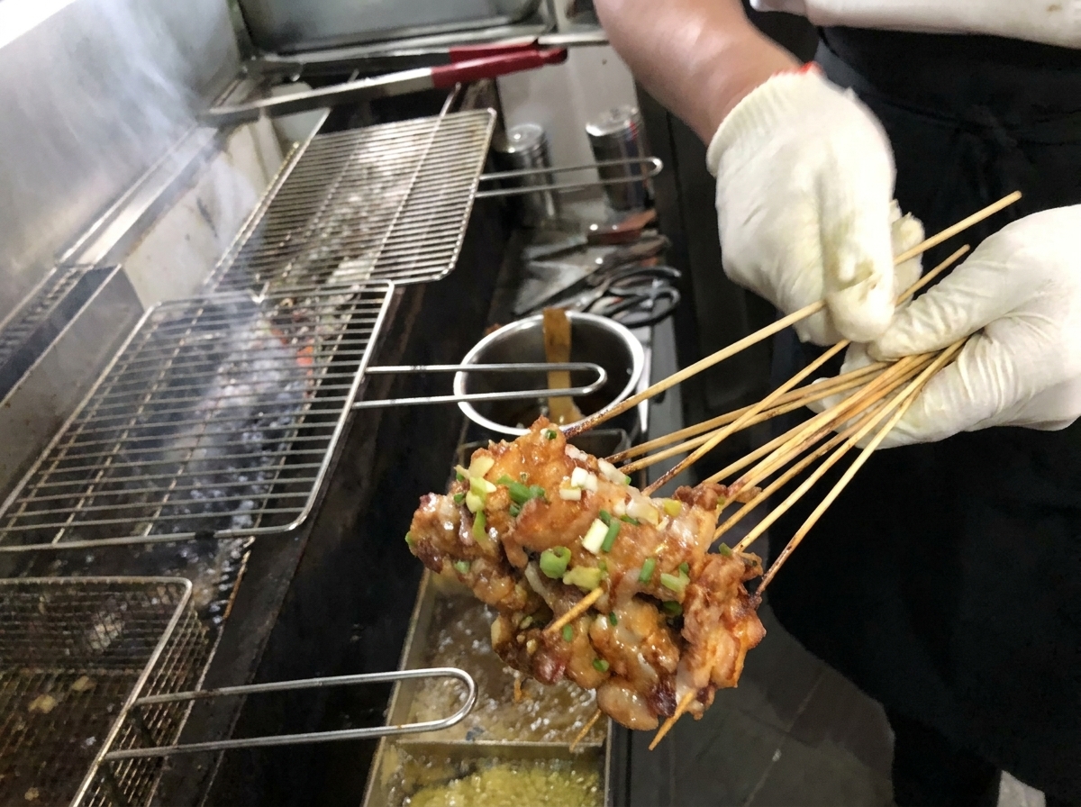 Gros plan dun pinceau appliquant une sauce brune et riche sur des brochettes de porc dorées sur un gril à charbon de bois.
