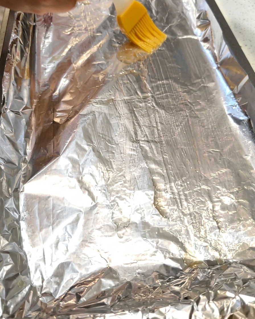 Un pinceau étalant de lhuile de cuisine sur une feuille de papier aluminium sur une plaque de cuisson.
