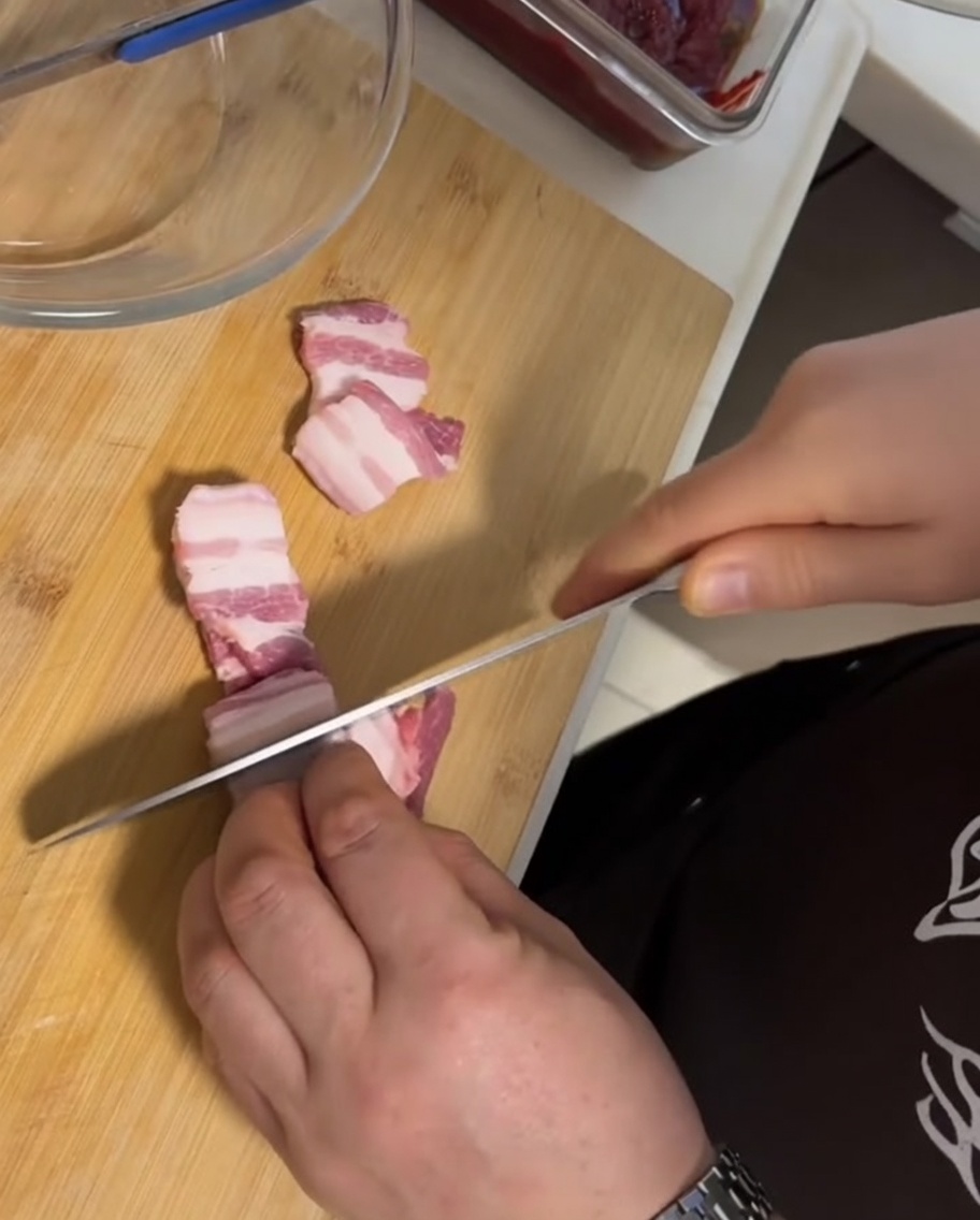 Tranches épaisses de poitrine de porc crue avec peau, disposées sur une planche à découper en bois à côté dun couteau.