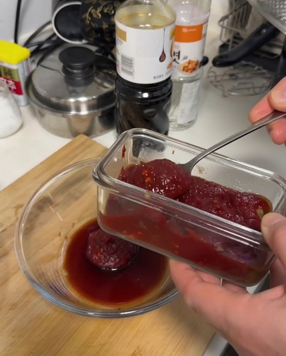 Une sauce rouge foncé épaisse mélangée à la cuillère dans un bol en verre transparent sur une surface en bois.