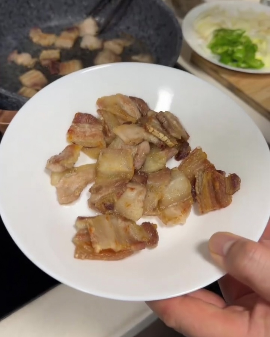Tranches de poitrine de porc en train de frire dans une poêle grise, montrant un extérieur doré et légèrement croustillant.