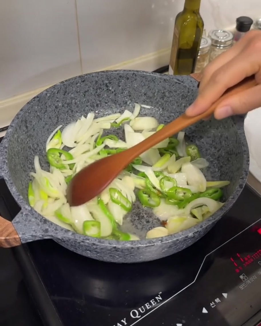 Oignons blancs tranchés, piments verts et gousses dail en train de sauter dans une poêle avec du gras fondu.