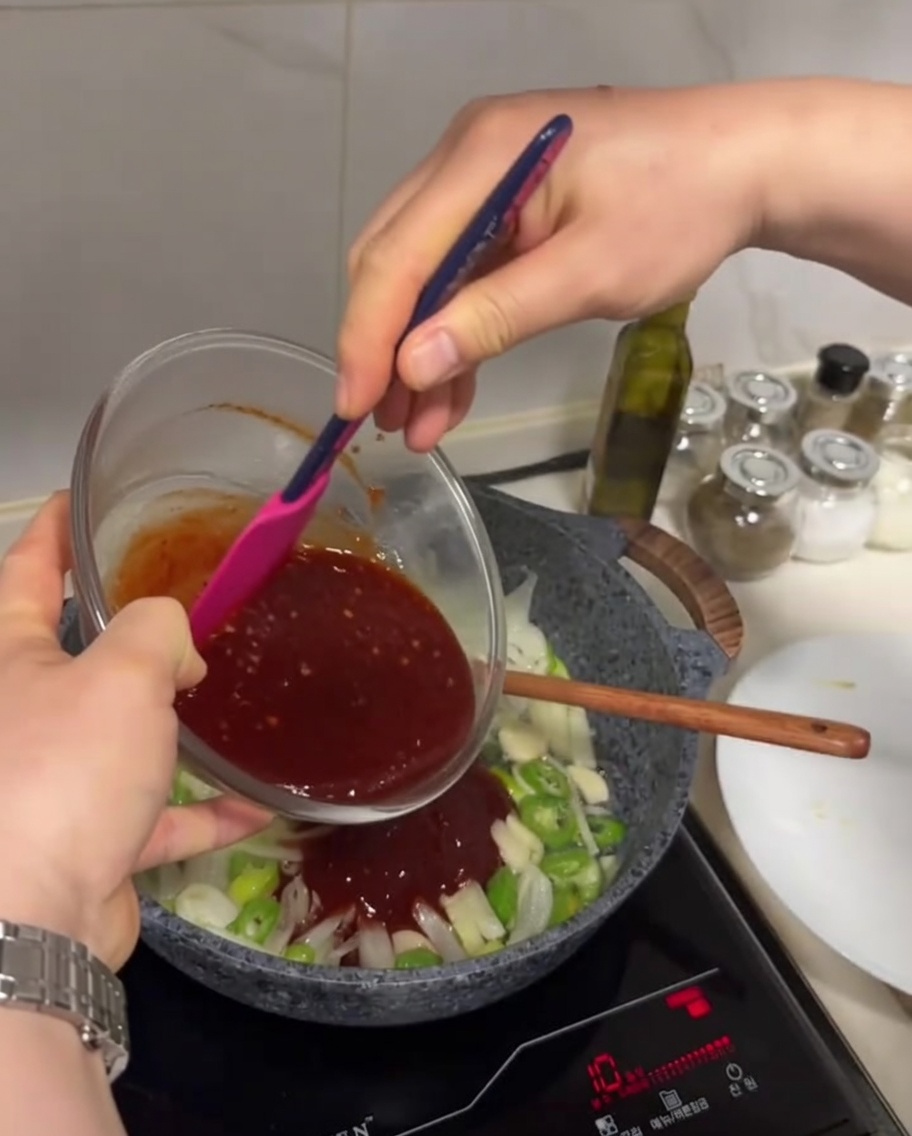 Sauce rouge foncé versée dun bol en verre dans une poêle contenant les légumes sautés.