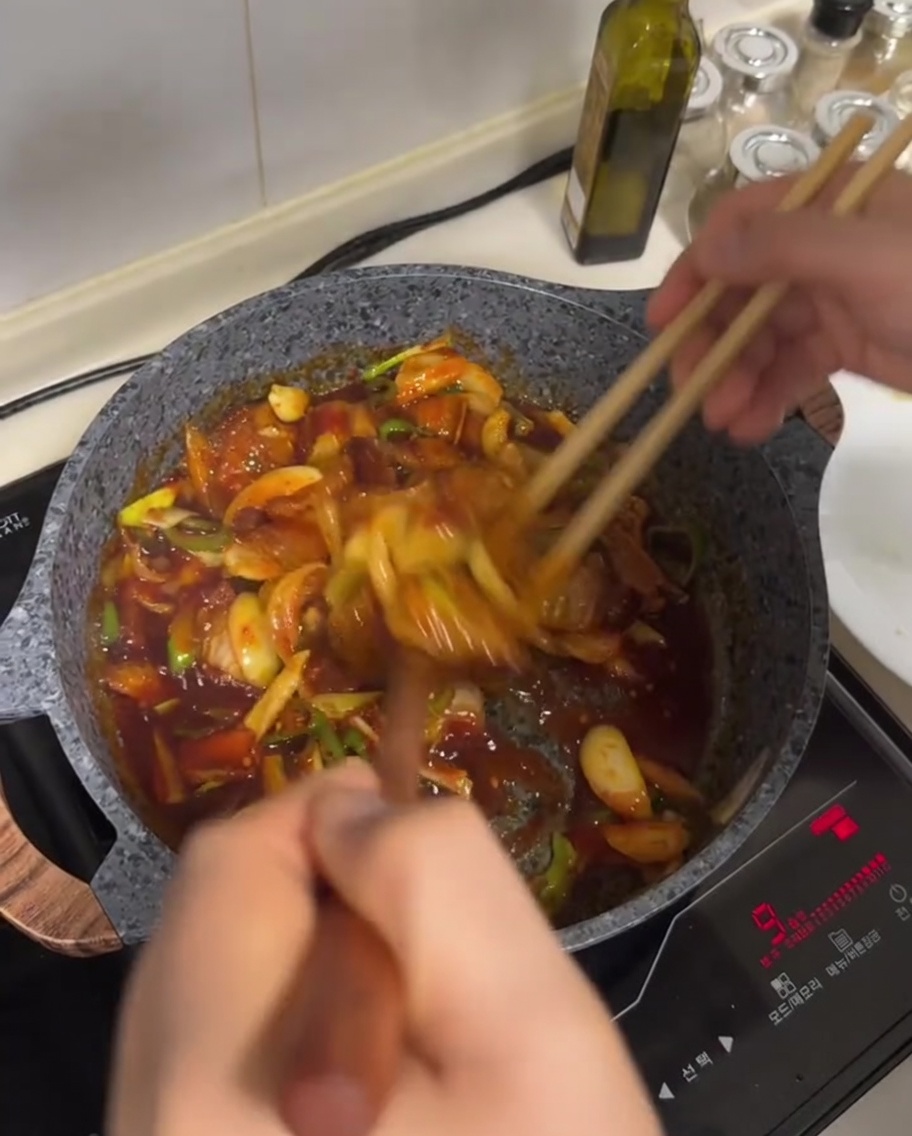 Sauté de poitrine de porc et légumes remués dans une sauce rouge dans une poêle.