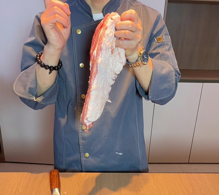 Gros plan sur la main dun chef coupant de la poitrine de porc crue en gros morceaux sur une planche à découper en bois.