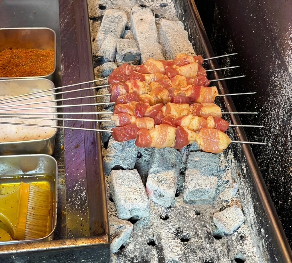 Brochettes de porc crues disposées sur un barbecue au charbon chaud, prêtes à cuire.