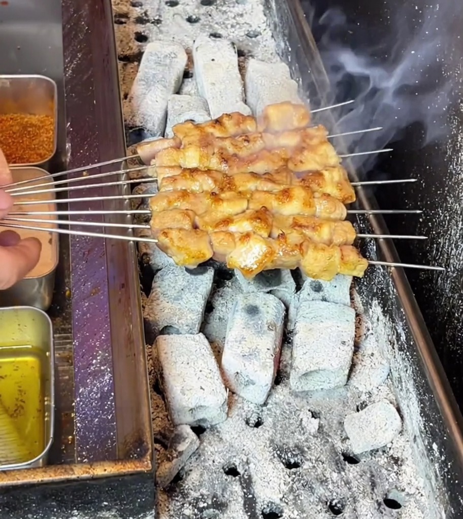 Brochettes de poitrine de porc devenant dorées tout en grésillant sur un barbecue au charbon fumant.