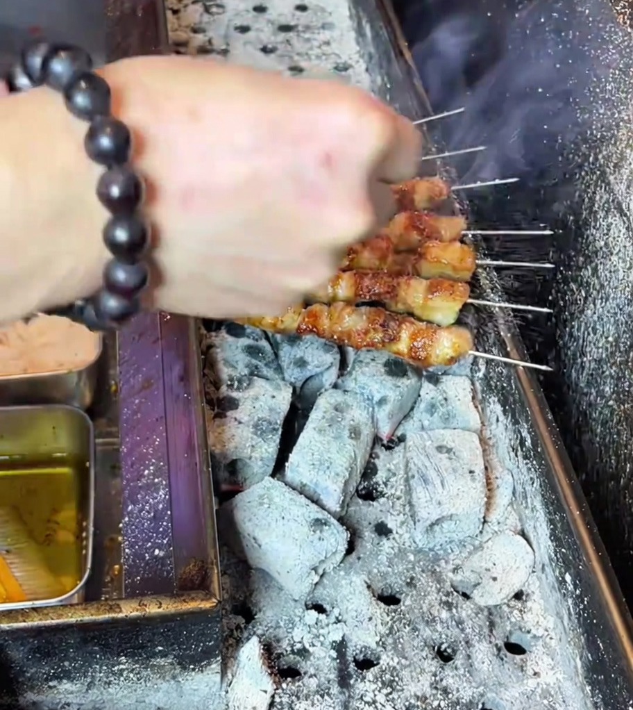 Une main saupoudrant de la poudre dassaisonnement sur des brochettes de porc grillées dorées sur le barbecue.