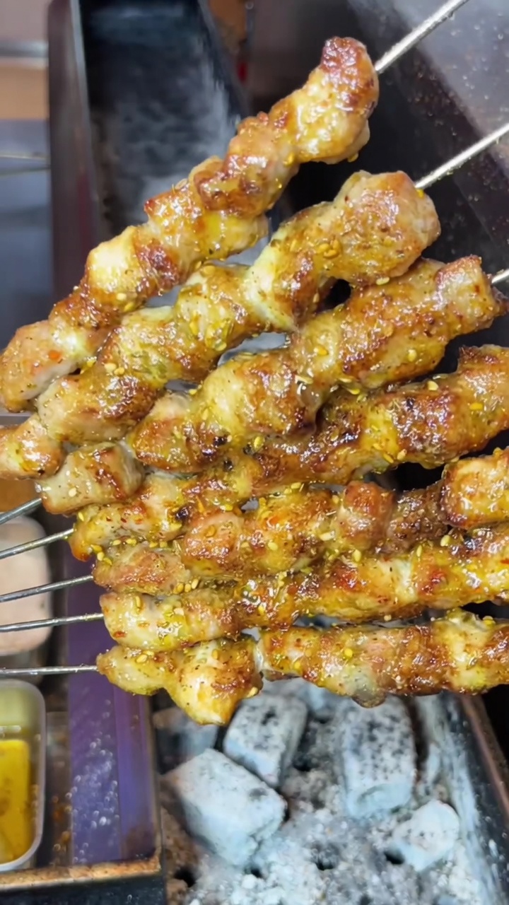 Brochettes de poitrine de porc grillées, dorées et croustillantes, saupoudrées dépices sur un barbecue au charbon.