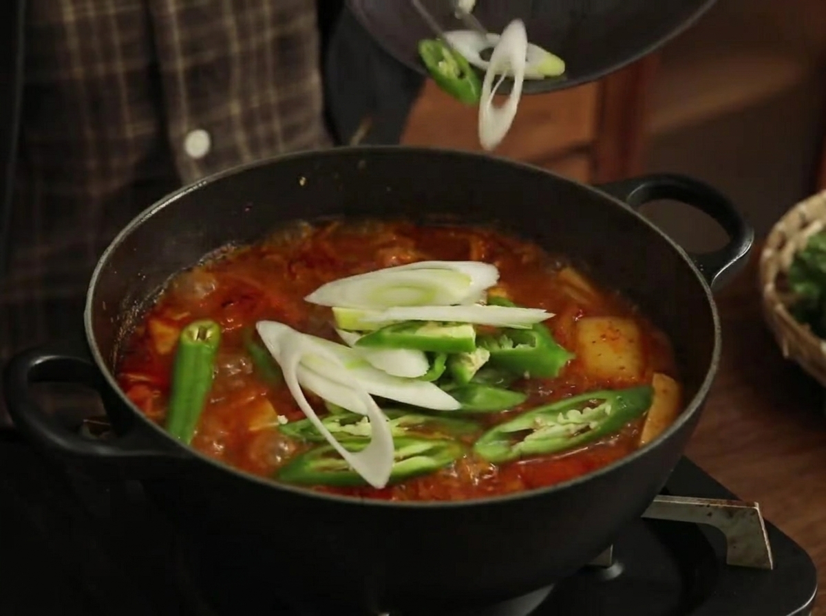 Tranches de poivrons verts et de poireaux ajoutées dans le ragoût bouillonnant.