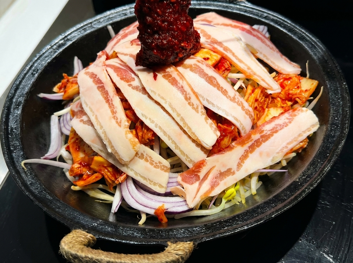 Une sauce coréenne rouge vif pour sauté versée sur une poêle de poitrine de porc et de légumes frais.