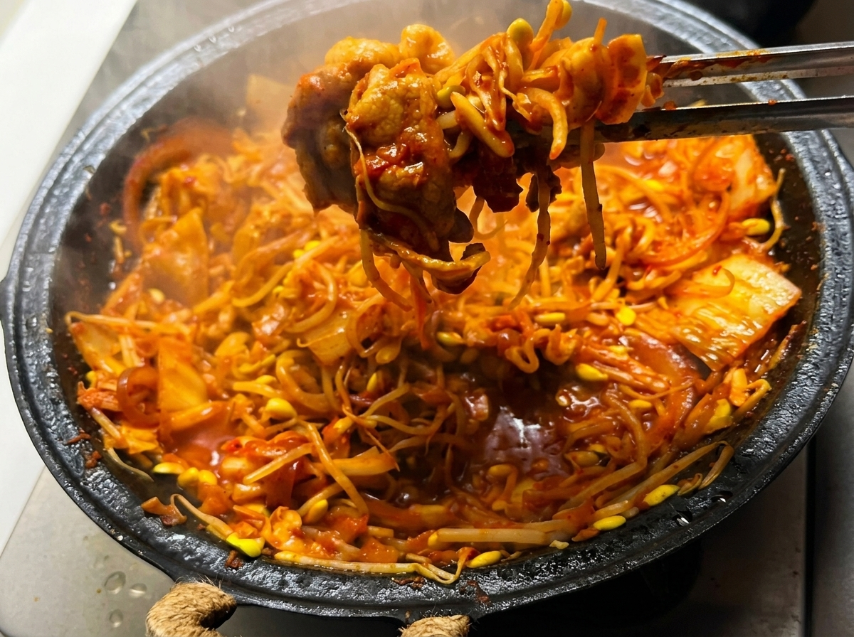 Le mélange de poitrine de porc au kimchi et pousses de soja sauté dans la poêle sur une flamme vive.