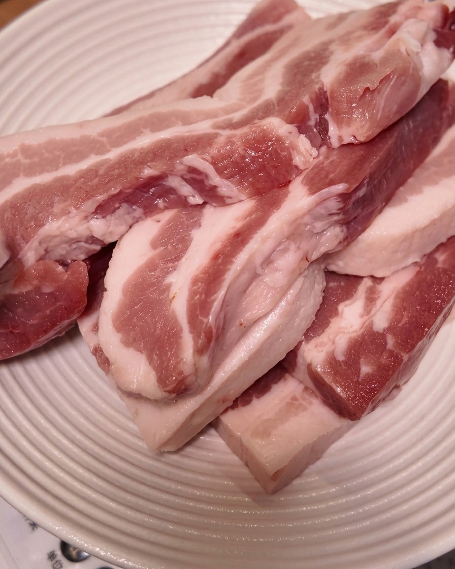 Tranches épaisses de poitrine de porc crue empilées sur une assiette blanche à rebords.