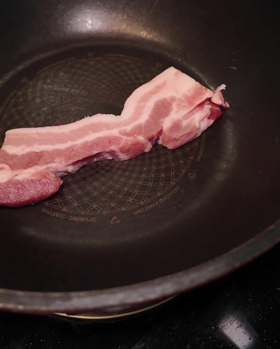 Une tranche épaisse de poitrine de porc crue placée dans une grande poêle noire.