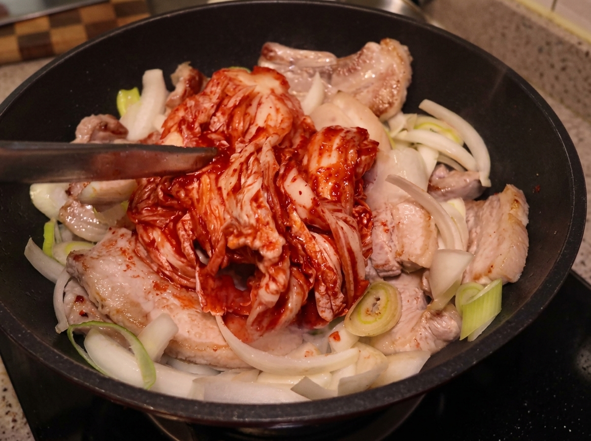 Un gros morceau de kimchi entier placé avec des pinces sur la poitrine de porc et les oignons.