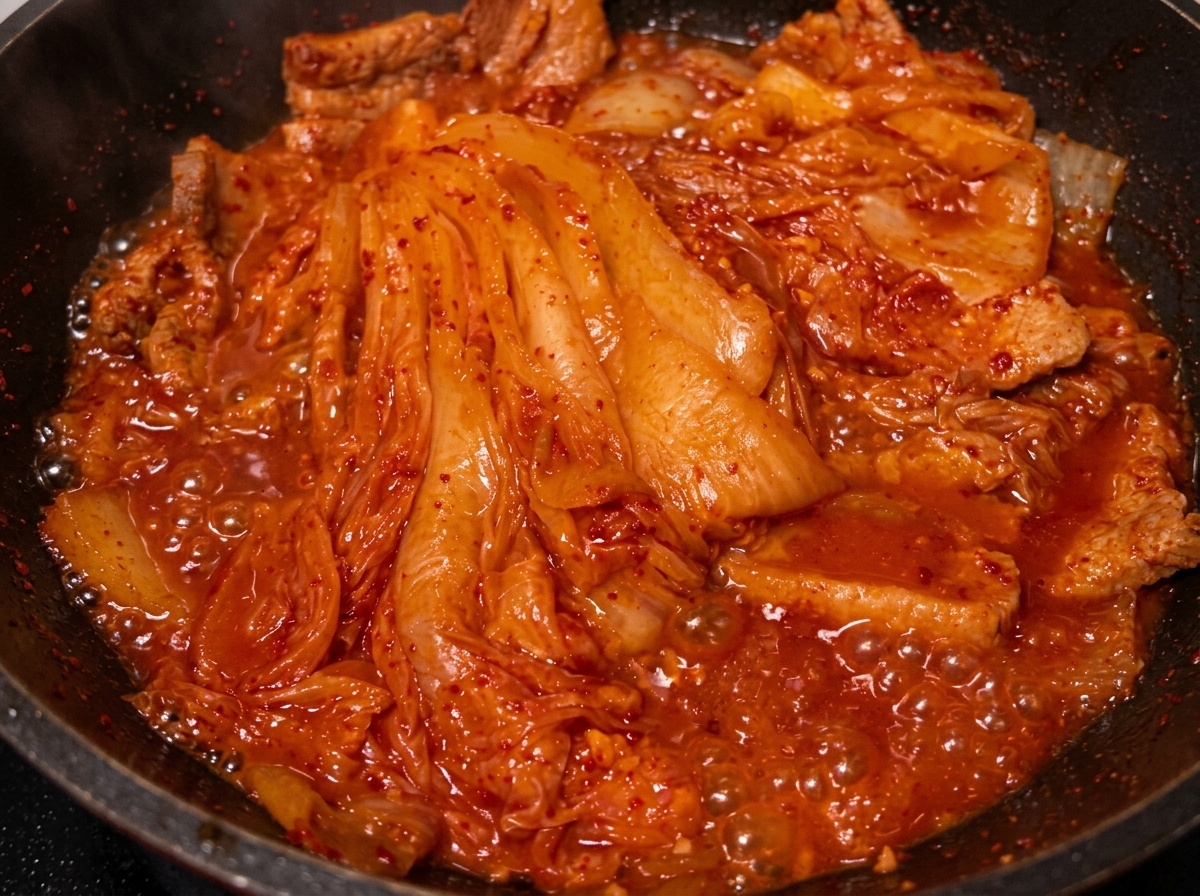 Huile versée depuis une cuillère dans la poêle avec le porc et le kimchi braisés.