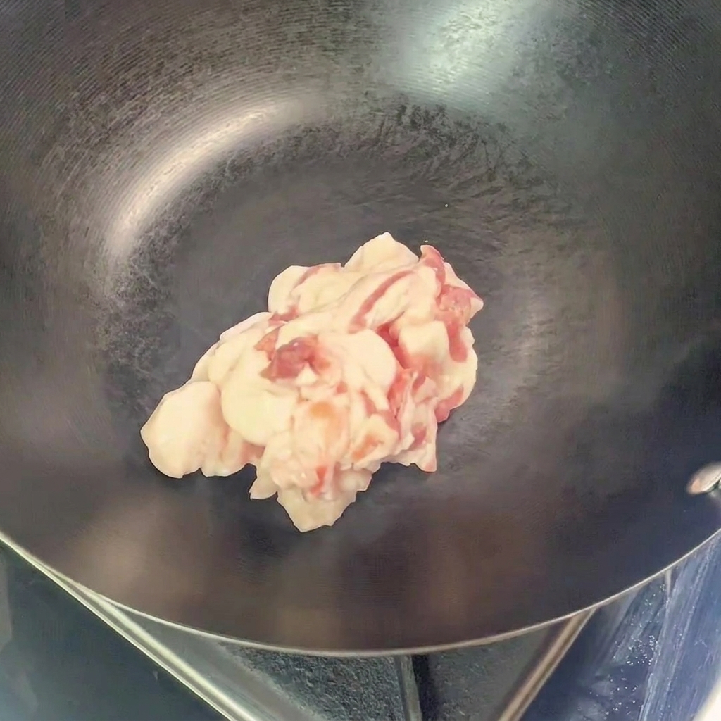 Un tas de morceaux de poitrine de porc crus déposés au centre dun wok vide et préchauffé.