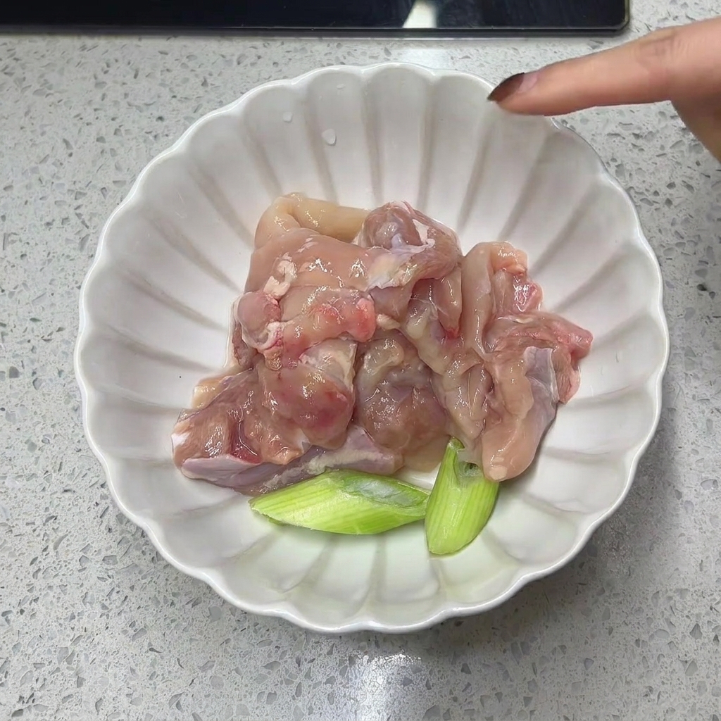 Cuisse de poulet désossée et tronçons doignons verts dans un bol blanc.