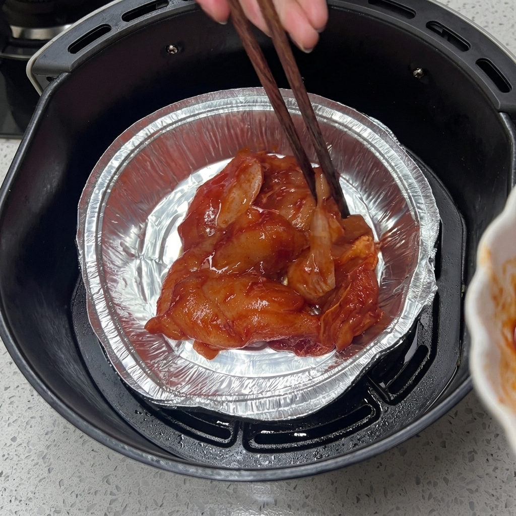 Baguettes en bois disposant le poulet mariné dans une barquette en aluminium dans un air fryer.