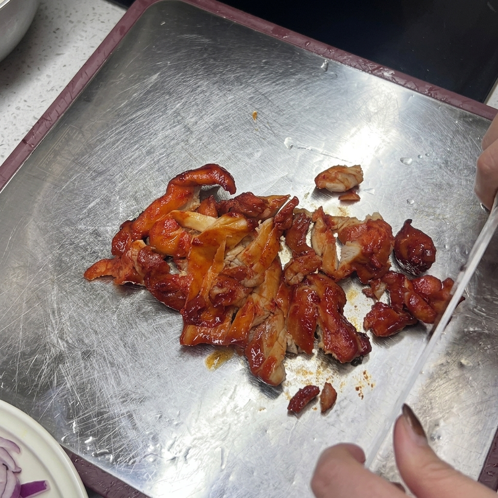Un couteau tranchant du poulet cuit, glacé et rouge-brun sur une planche à découper métallique.
