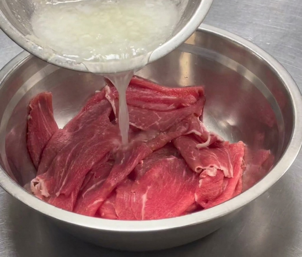 Purée aromatique versée dans un grand bol en inox contenant des tranches de bœuf.