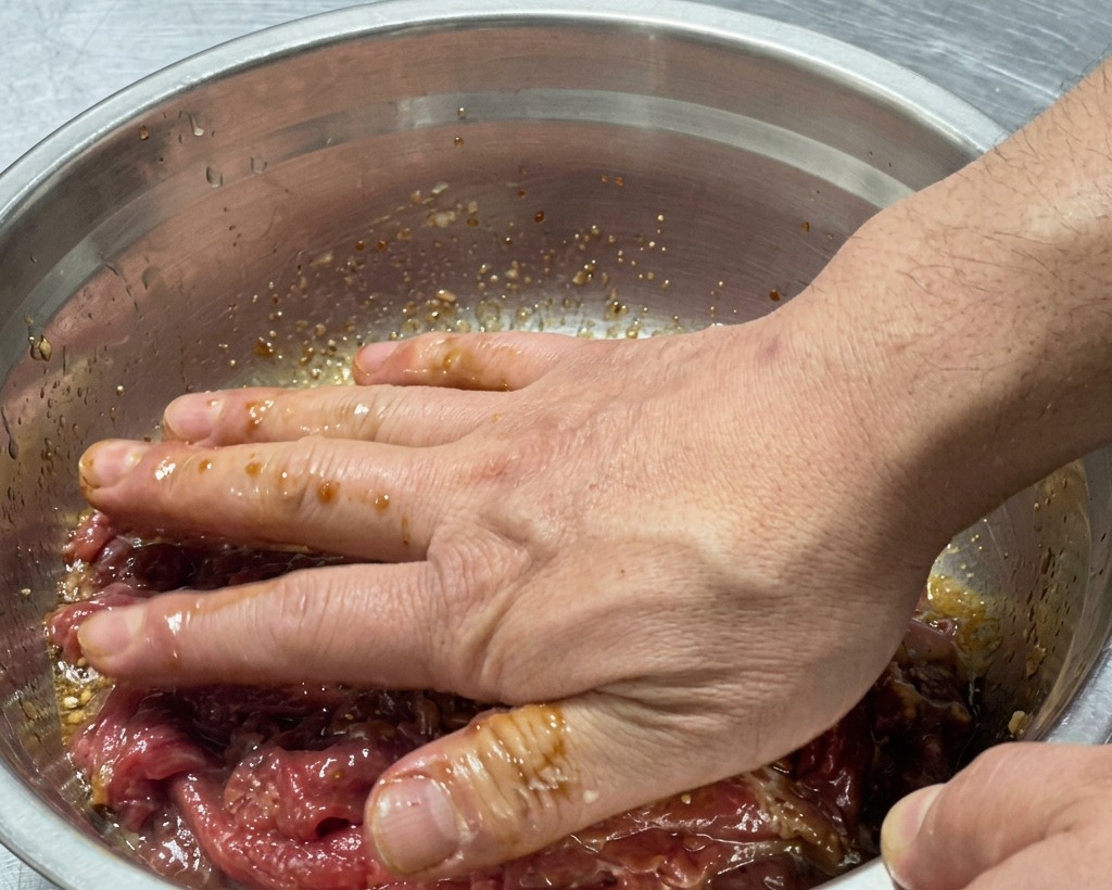 Mains mélangeant soigneusement le bœuf cru avec la marinade dans le bol.