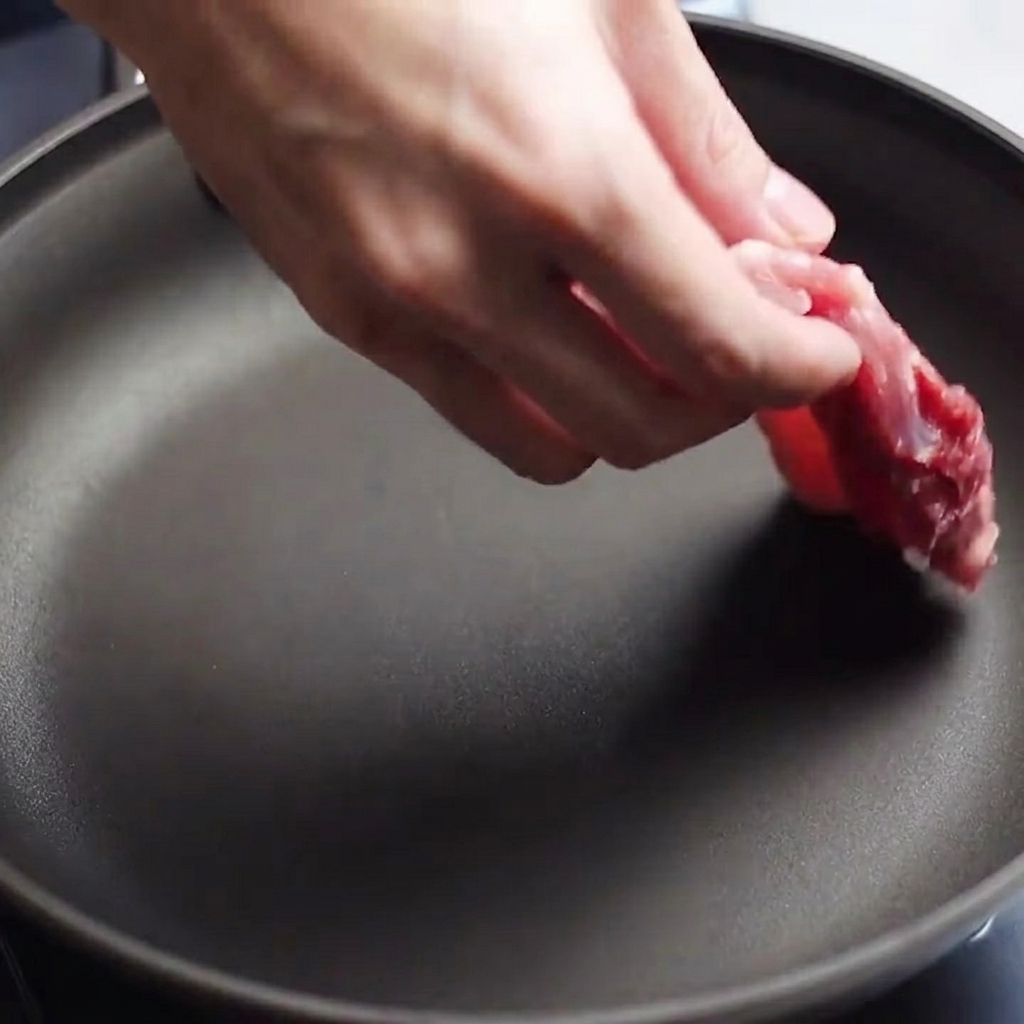 Des tranches de poitrine de porc crue et assaisonnées déposées dans une poêle préchauffée.