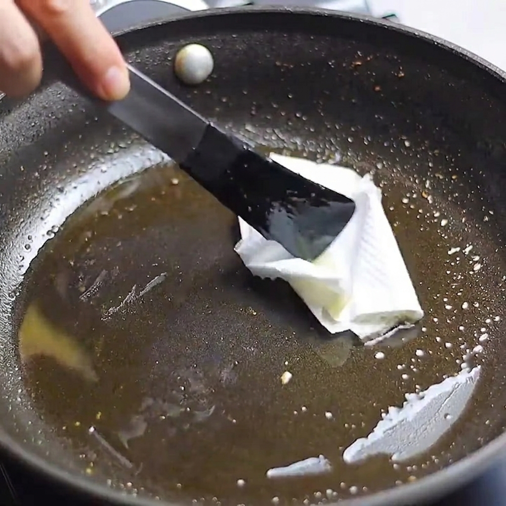 Un essuie-tout de cuisine tenu par des pinces utilisé pour essuyer lexcès de gras dune poêle.